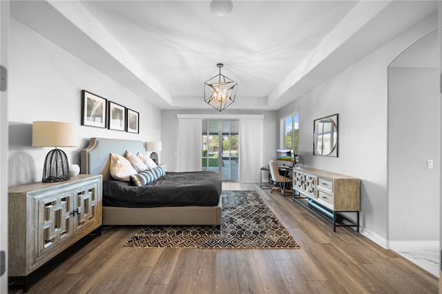 bedroom featuring arched walkways, baseboards, a raised ceiling, wood finished floors, and a chandelier