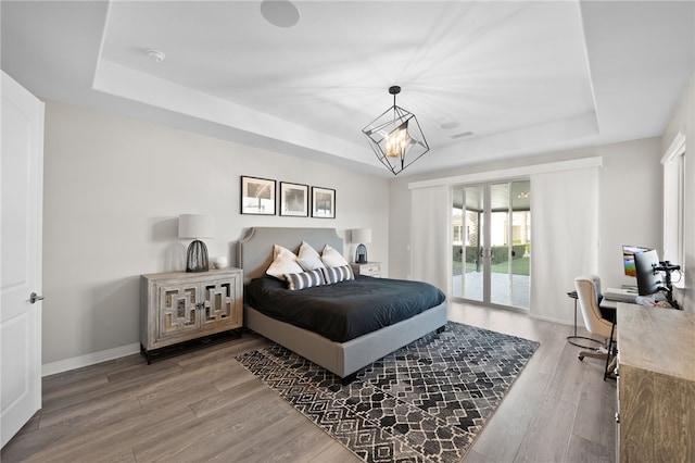 bedroom featuring a tray ceiling, wood finished floors, a chandelier, access to outside, and baseboards