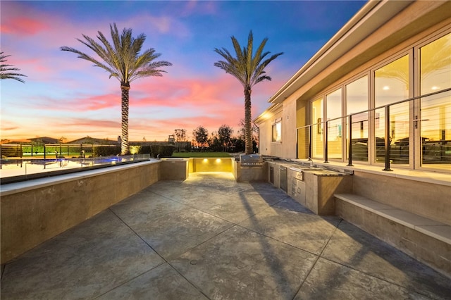 patio terrace at dusk featuring exterior kitchen, a water view, and a grill