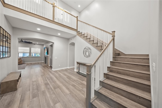 staircase with arched walkways, a high ceiling, wood finished floors, a ceiling fan, and baseboards