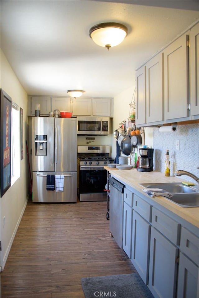 kitchen with dark wood-style flooring, stainless steel appliances, light countertops, backsplash, and a sink