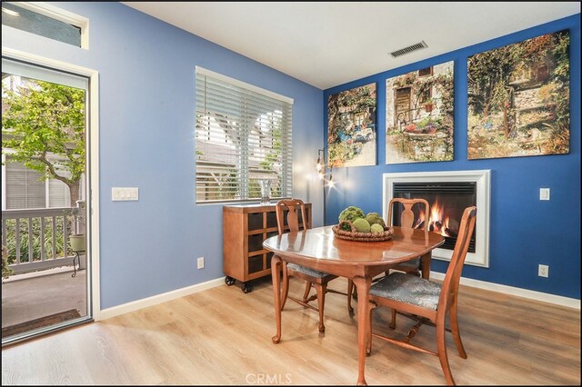 dining room with a glass covered fireplace, visible vents, light wood-style flooring, and baseboards