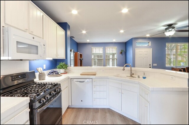 kitchen with a peninsula, white appliances, tile counters, and a healthy amount of sunlight