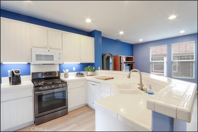 kitchen with white appliances, tile countertops, light wood-style flooring, a peninsula, and a sink