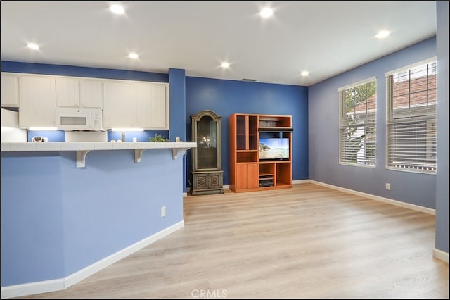 kitchen featuring white cabinets, tile countertops, white microwave, a breakfast bar, and light wood-style floors