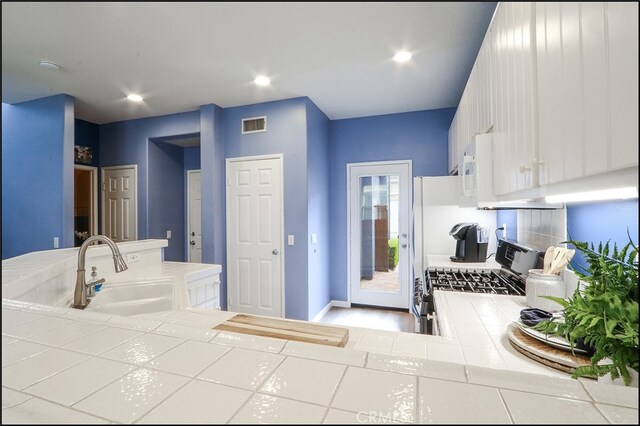 kitchen with visible vents, tile countertops, stainless steel gas range, white cabinetry, and a sink