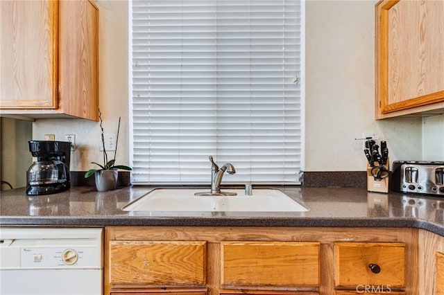 kitchen with dark countertops, white dishwasher, and a sink