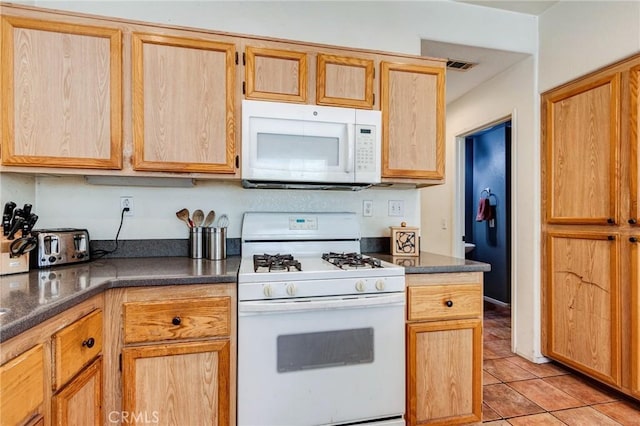 kitchen with dark countertops, white appliances, visible vents, and light tile patterned flooring