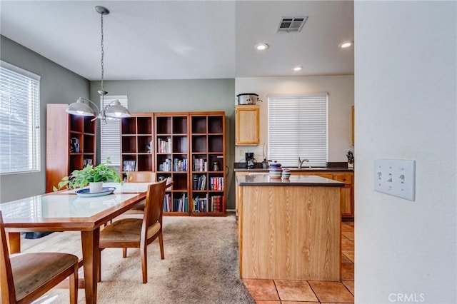 kitchen with light brown cabinets, a sink, visible vents, hanging light fixtures, and dark countertops