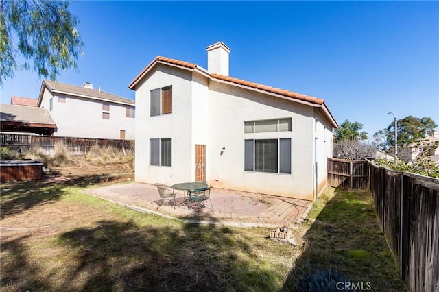 rear view of house with a patio, a fenced backyard, a tile roof, stucco siding, and a chimney