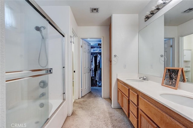 bathroom featuring a spacious closet, double vanity, bath / shower combo with glass door, and a sink