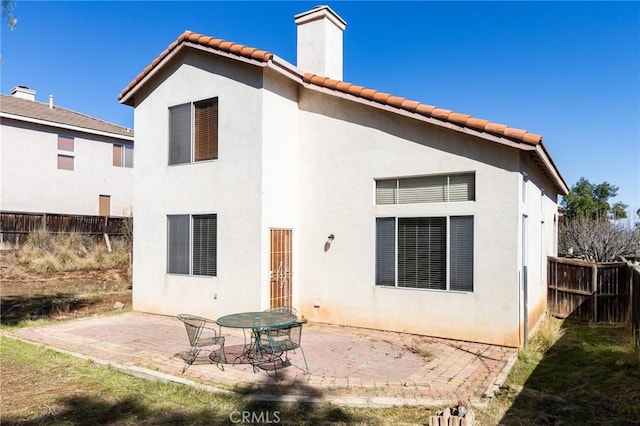 rear view of property with a tile roof, a patio, a chimney, stucco siding, and fence