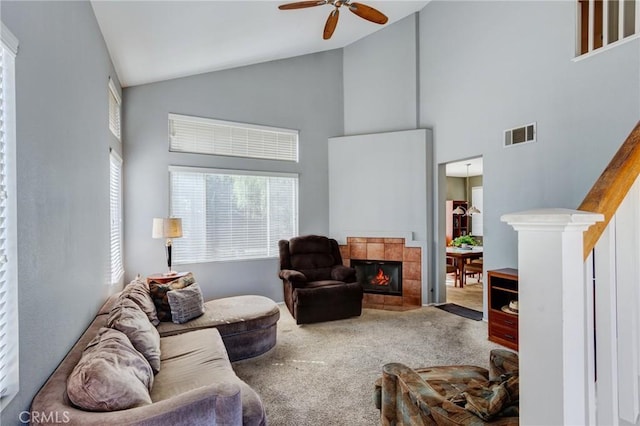 carpeted living area with ceiling fan, high vaulted ceiling, a fireplace, visible vents, and stairs