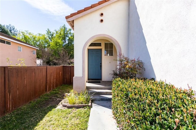 view of exterior entry featuring a tile roof, fence, and stucco siding