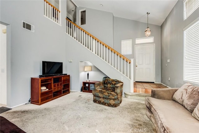 living area with light carpet, baseboards, visible vents, a towering ceiling, and stairs