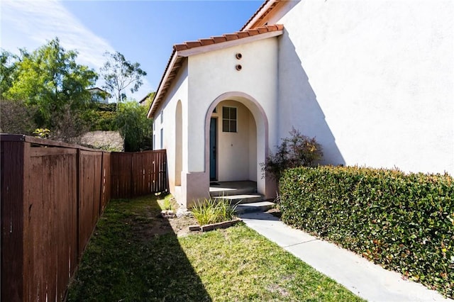 entrance to property featuring a tile roof, fence, and stucco siding