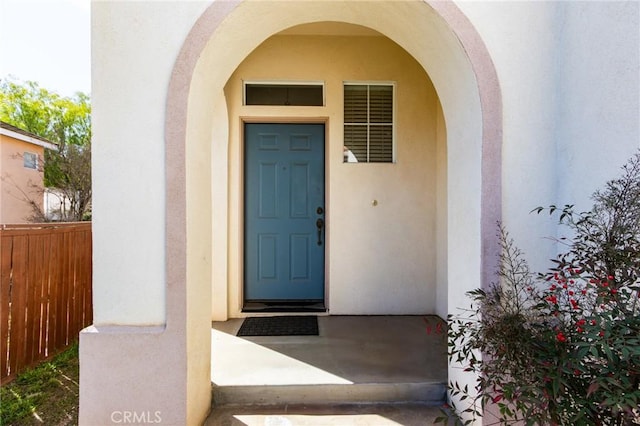 doorway to property featuring fence and stucco siding