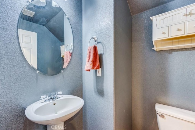 half bath featuring a textured wall, a sink, and toilet