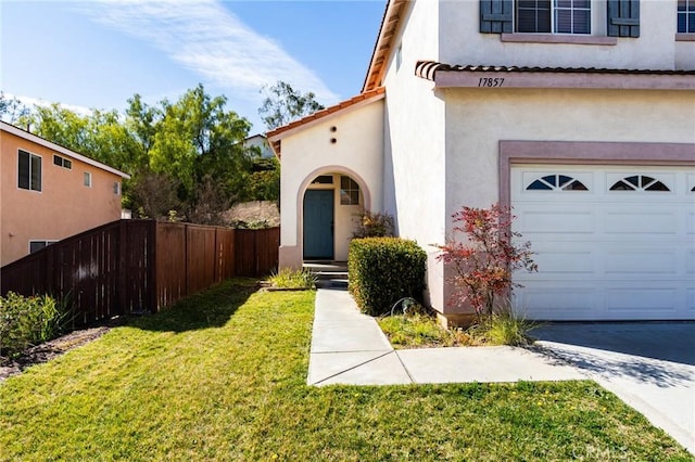 doorway to property with an attached garage, fence, a tile roof, a lawn, and stucco siding