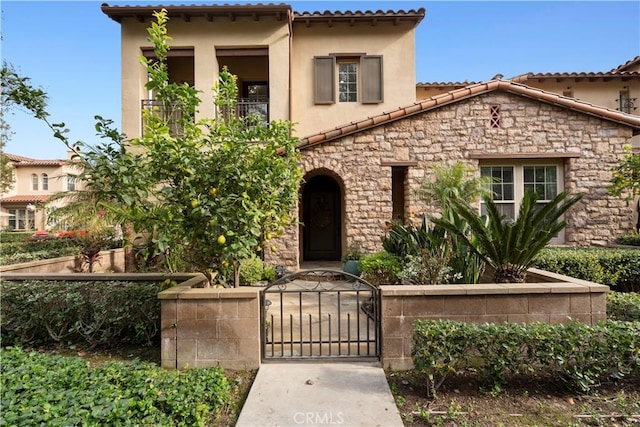 mediterranean / spanish-style home featuring stone siding, fence, a gate, and stucco siding