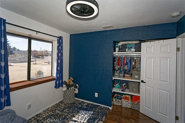 bedroom with dark wood-style floors, visible vents, a textured wall, and baseboards