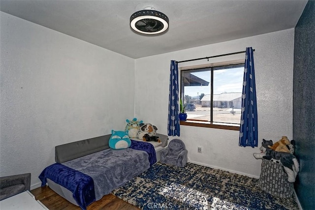 bedroom featuring a textured wall, wood finished floors, and baseboards