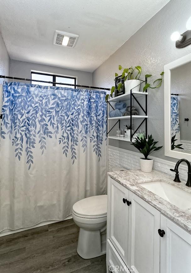 full bathroom featuring visible vents, a textured wall, toilet, wood finished floors, and vanity