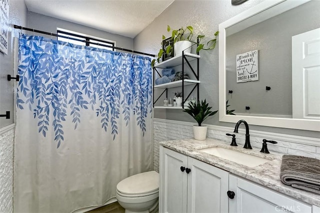 bathroom featuring toilet, a textured wall, a shower with curtain, and vanity