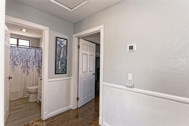 hall with a textured wall, dark wood finished floors, and wainscoting