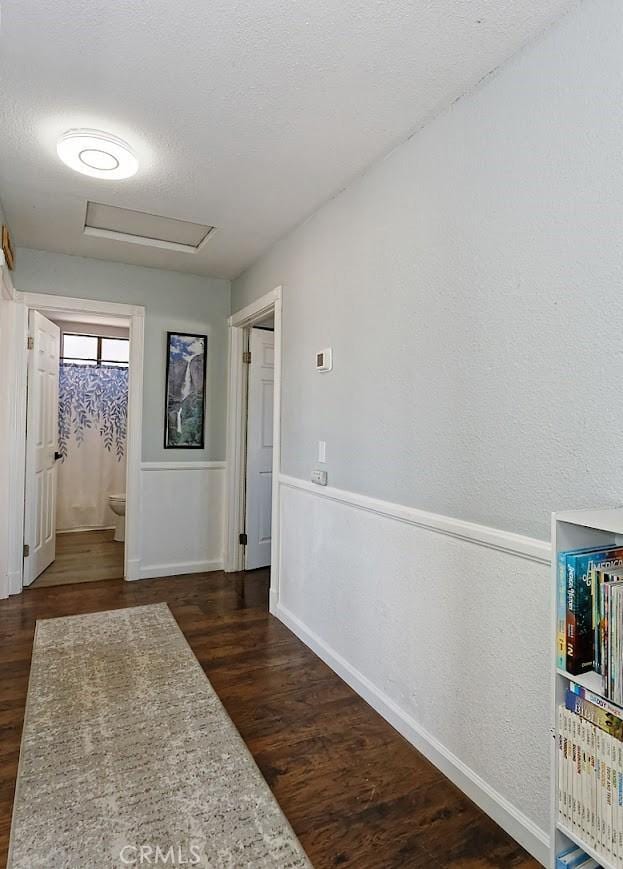 corridor featuring attic access, dark wood finished floors, and a textured ceiling