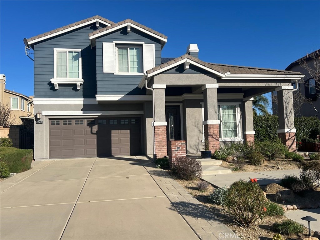 craftsman-style home with an attached garage, brick siding, driveway, and a chimney