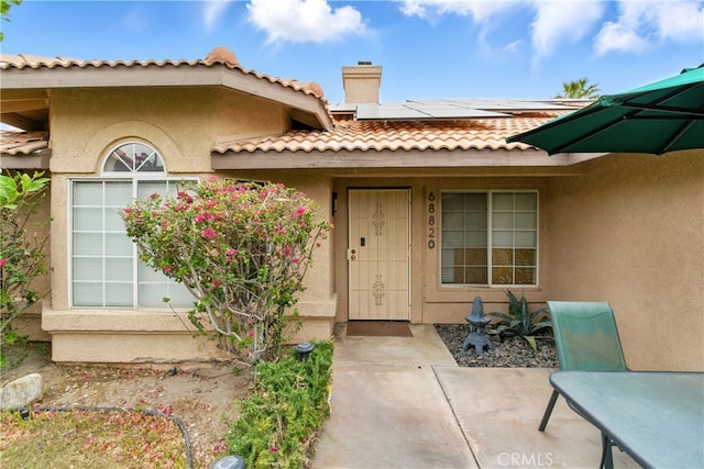 68820 San Felipe Rd, Cathedral City, CA 92234 - view of exterior entry featuring roof mounted solar panels, stucco siding, a chimney, and a tiled roof