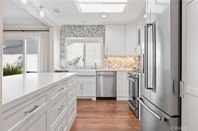 kitchen featuring a skylight, a sink, high quality appliances, white cabinetry, and dark wood finished floors