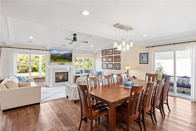 dining area featuring lofted ceiling with beams, recessed lighting, wood finished floors, and a glass covered fireplace