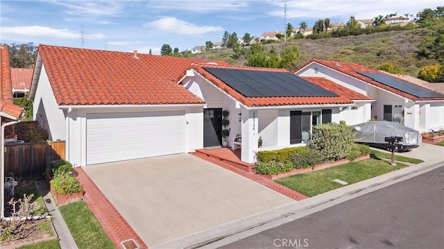 mediterranean / spanish-style house featuring an attached garage, fence, a tile roof, concrete driveway, and roof mounted solar panels