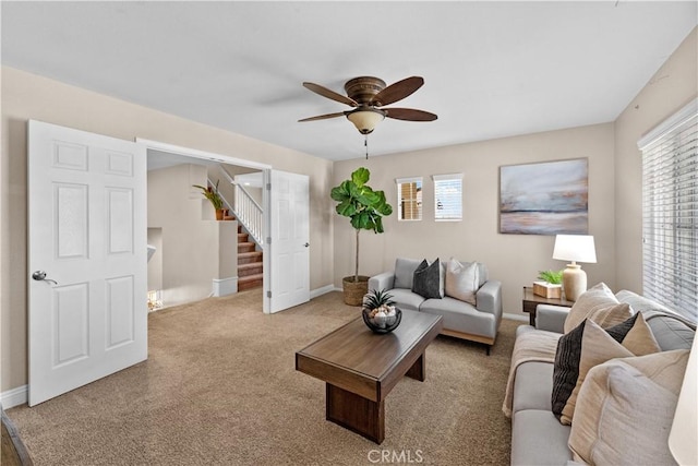 carpeted living area with baseboards, stairs, a ceiling fan, and a wealth of natural light