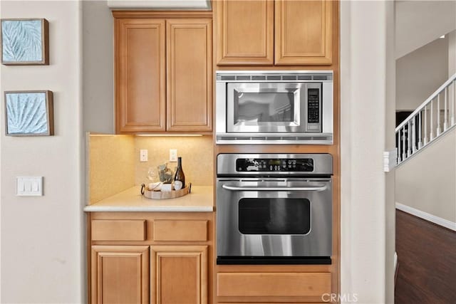 kitchen featuring baseboards, dark wood-type flooring, stainless steel appliances, light countertops, and backsplash