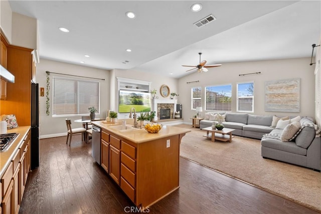 kitchen with stainless steel appliances, visible vents, open floor plan, a sink, and a stone fireplace