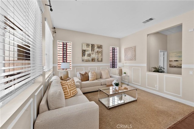 living room with visible vents, a decorative wall, and wainscoting