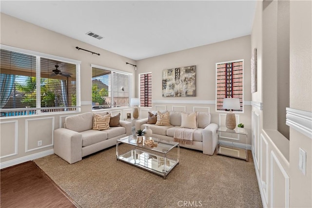 living area with a wainscoted wall, wood finished floors, visible vents, and a decorative wall