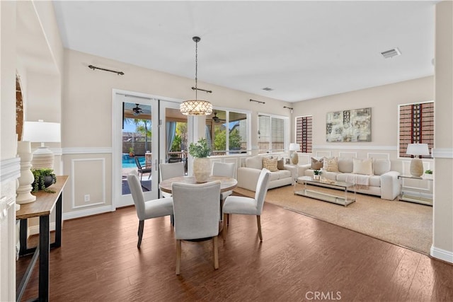 dining space with a wainscoted wall, visible vents, a decorative wall, dark wood-type flooring, and a chandelier