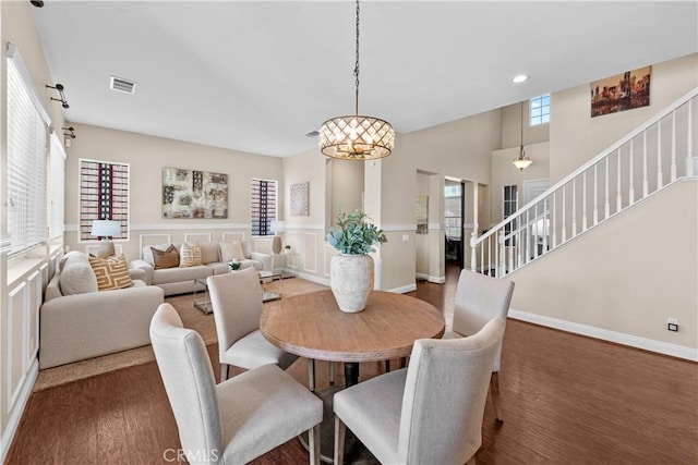 dining space with a high ceiling, wood finished floors, visible vents, baseboards, and stairway