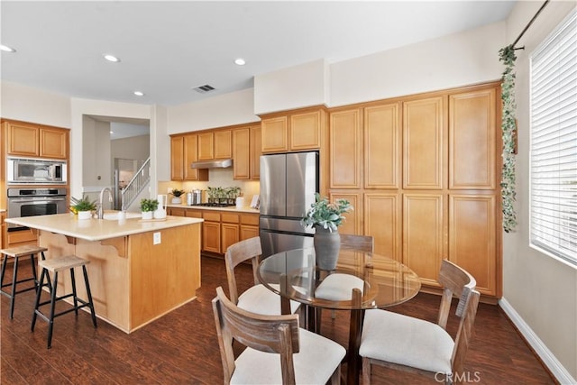 kitchen with visible vents, dark wood-style floors, a kitchen island with sink, stainless steel appliances, and light countertops