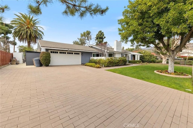 ranch-style house featuring an attached garage, fence, a front lawn, and decorative driveway