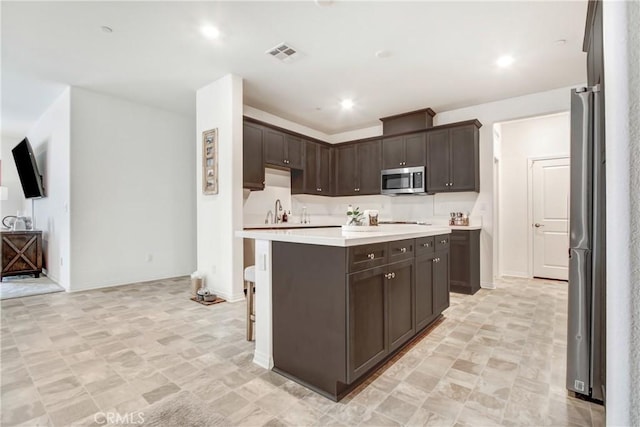 kitchen featuring dark brown cabinetry, visible vents, a center island, stainless steel appliances, and light countertops