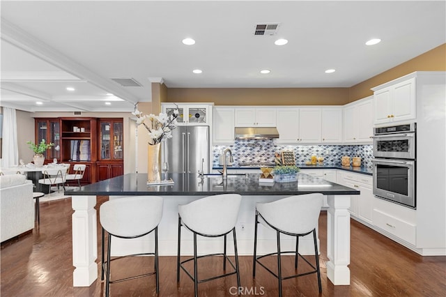 kitchen with dark countertops, white cabinetry, appliances with stainless steel finishes, and a large island with sink