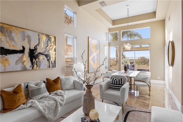 living room featuring a notable chandelier, a towering ceiling, visible vents, baseboards, and a tray ceiling