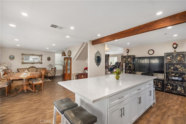 kitchen featuring wood finished floors, visible vents, white cabinets, open floor plan, and beam ceiling