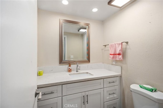 half bathroom featuring toilet, vanity, and recessed lighting