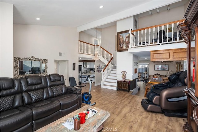 living area with recessed lighting, visible vents, wood finished floors, high vaulted ceiling, and stairs